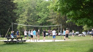 A group of people gathered around a volleyball net in a park with picnic tables and cars in the background. - Studio Suite with 2 beds - Located at the Heart of Promised Land State Park  (Greentown)
