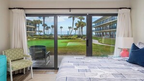 Un dormitorio con una cama grande, una silla, un escritorio y vistas a un campo de golf y edificios.