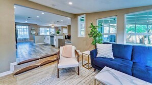 A spacious living area with a blue sofa, a white armchair, and a small side table. A large window provides a view of the outdoors. - San Antonio Retreat: Pool, Hot Tub & Pickleball (San Antonio)
