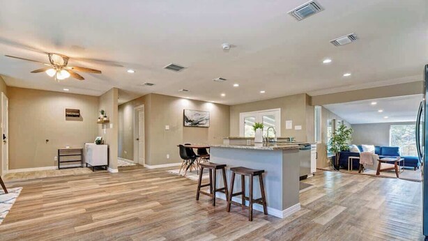 A spacious living area with a wooden floor, a ceiling fan, and a bar area with stools. - San Antonio Retreat: Pool, Hot Tub & Pickleball (San Antonio)