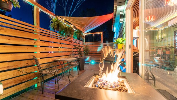 Eine Terrassengruppe mit Feuerstelle, Holzdeck, Metallstühlen und hängenden Pflanzgefäßen.
