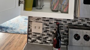 A kitchen with a cabinet containing various glassware, a bottle of wine, and a modern stove. - Sweet 3 Bedroom, Walk to Main St! (Independence)