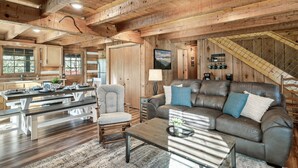 A rustic cabin interior with a wooden dining area, a leather sofa, and a staircase.