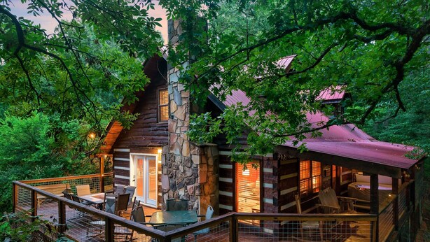 A log cabin with a stone chimney, wooden deck, and outdoor seating area.
