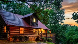 A rustic log cabin with a metal roof, a porch, and a staircase leading to a deck.