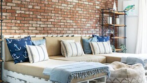 Una habitación acogedora con pared de ladrillo, cama blanca con almohadas a rayas y una estantería de madera con adornos.