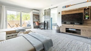 Un dormitorio moderno con una cama grande, un televisor instalado en una pared de madera, un ventanal corredero que da a un balcón y un escritorio con una silla.