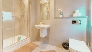 Un baño moderno con cabina de ducha de vidrio, un lavabo blanco y un inodoro.