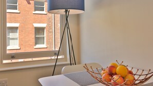 Una habitación con ventana, lámpara y frutero sobre una mesa.