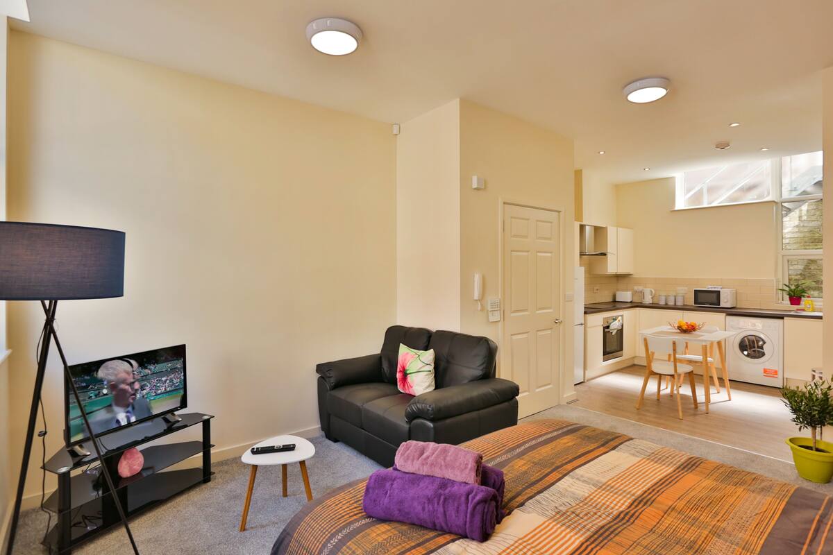 A modern living room with a flat-screen TV, a sofa, a small coffee table, and a patterned rug.