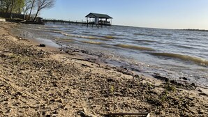 A beach with a wooden pier extending into the water, a small shelter at the end, and sparse vegetation.