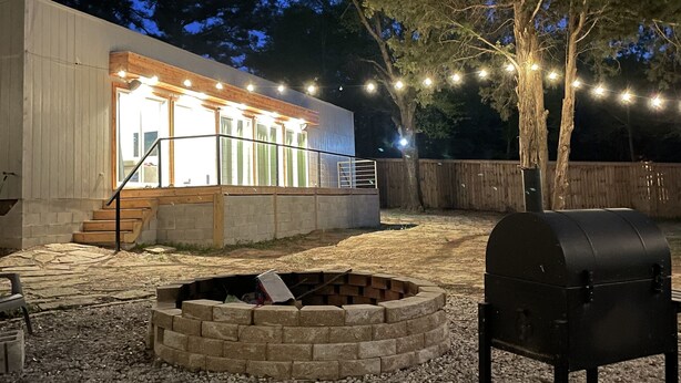 A modern outdoor patio area with a barbecue grill, a fire pit, and string lights.