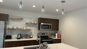 A modern kitchen with a stainless steel refrigerator, a microwave, a stove, and a sink. There are wooden cabinets and marble countertops.