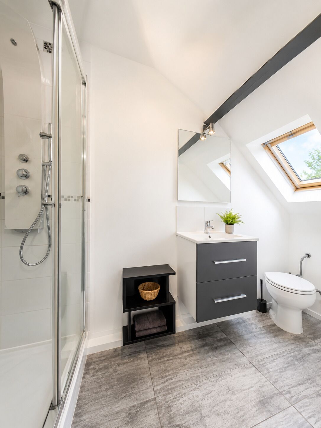 Une salle de bain moderne avec une douche à parois de verre, un meuble-lavabo avec un miroir et une fenêtre de toit.