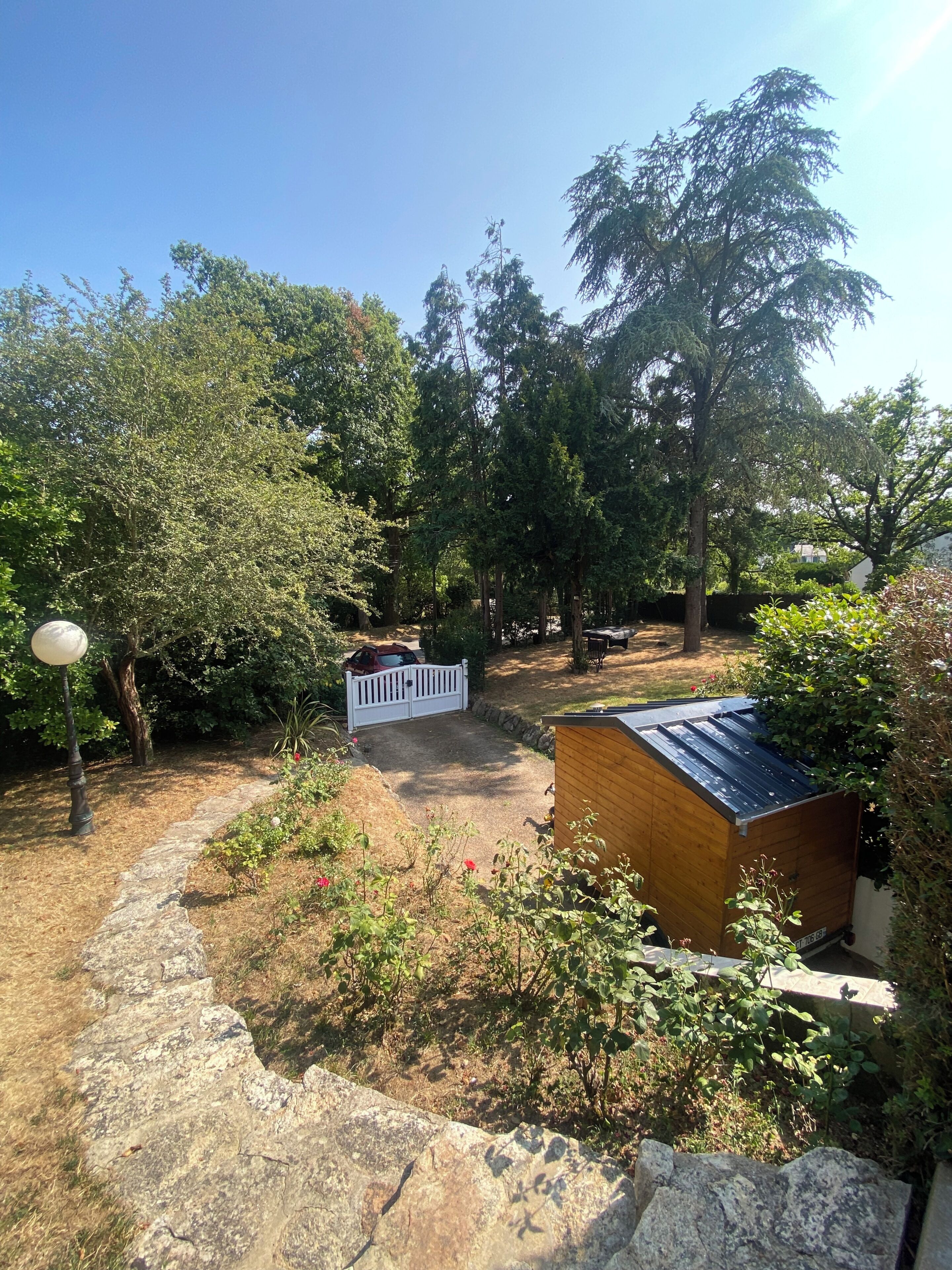 Ein Garten mit einem Kiesweg, einem Holzschuppen und einem weißen Zaun.