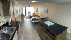 A kitchen with a black countertop, stainless steel sink, and wooden cabinets. There is a dining area with a table and chairs, and a window providing natural light. - Best Views in Orange Beach!!  (Orange Beach)