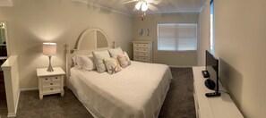 A bedroom with a bed, a nightstand, a dresser, a ceiling fan, a window with blinds, and a TV stand with a remote control. - Best Views in Orange Beach!! (Orange Beach)