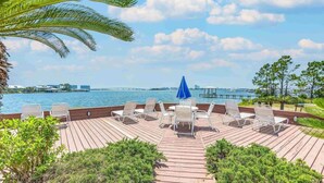 A wooden deck with lounge chairs and a blue umbrella, overlooking a body of water with a bridge in the distance. - Best Views in Orange Beach!!  (Orange Beach)