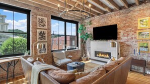 A living room with a fireplace, leather sofa, and a large window overlooking a cityscape.