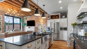 A modern kitchen with a large island, stainless steel appliances, and a brick wall.