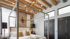 A four-poster bed with a wooden headboard, a bench, and a large window with curtains.