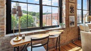 A room with a large window, a wooden desk, two chairs, and a lamp.