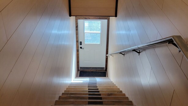 A wooden staircase with a metal handrail leading to a door with a small window.