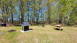 A backyard with a barbecue grill, a picnic table, and a fire pit.