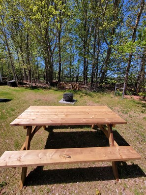 A wooden picnic table in a grassy area with trees in the background.