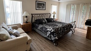 Een slaapkamer met een bed, een stoel, een nachtkastje, een plafondventilator en een raam met zonwering.