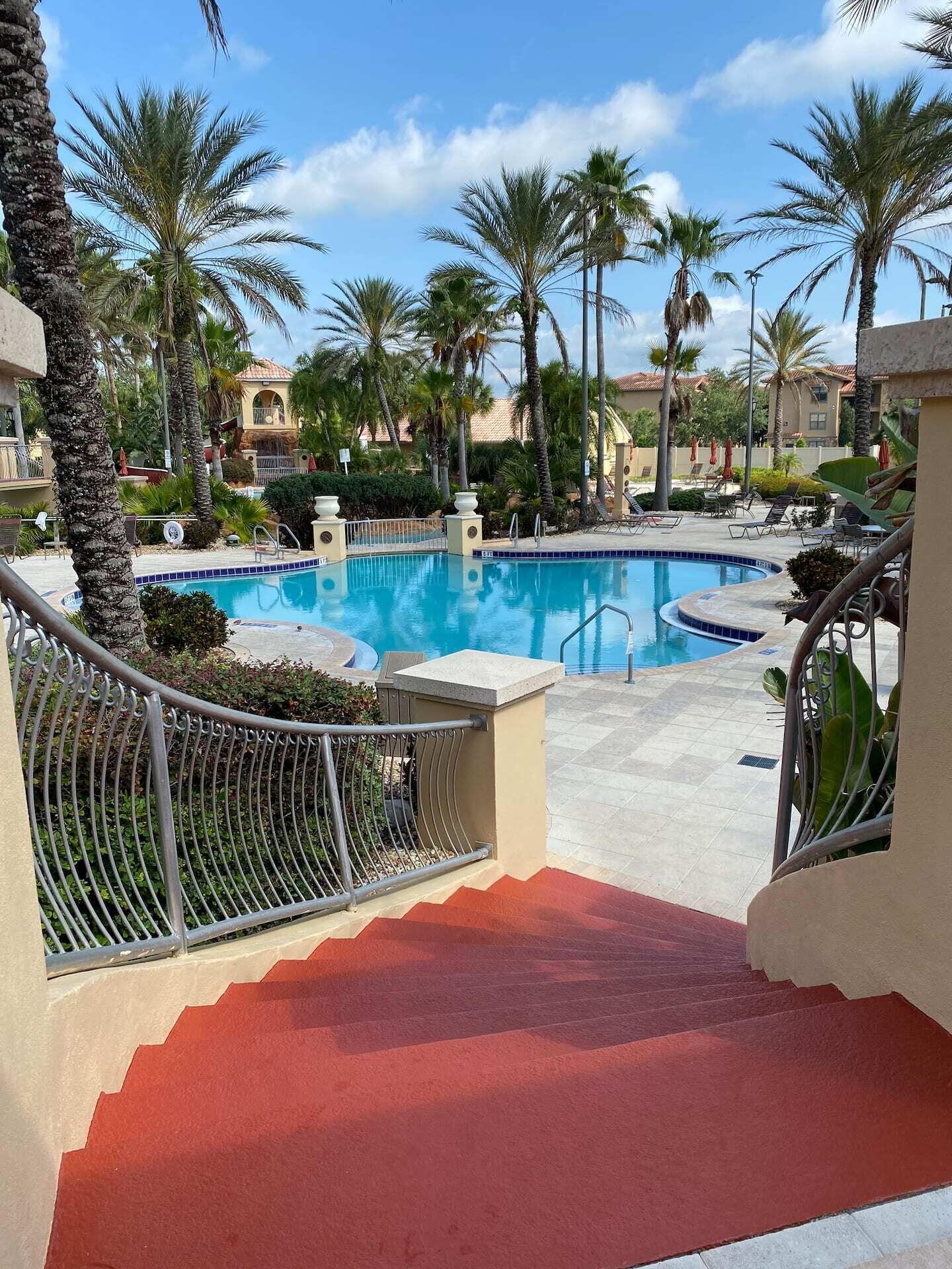 A swimming pool with a red-tiled deck, surrounded by palm trees and lounge chairs.