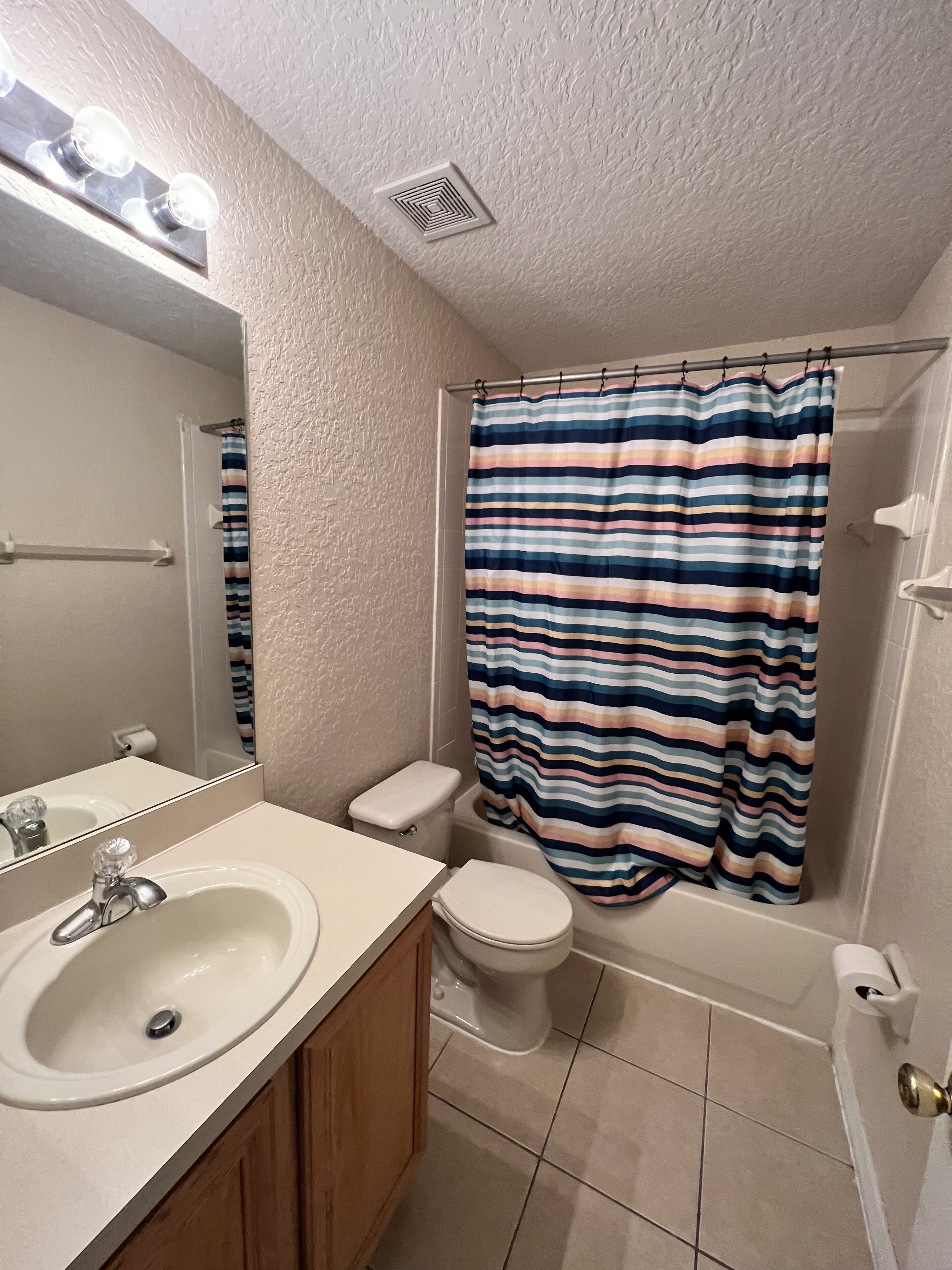 A bathroom with a white sink, a toilet, a shower curtain, and a mirror.