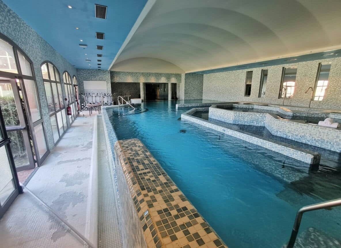 Ein Hallenbad mit klarem Wasser, gefliestem Boden und einer Sitzgelegenheit mit Schachbrettmuster.