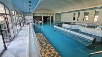 Ein Hallenbad mit klarem Wasser, gefliestem Boden und einer Sitzgelegenheit mit Schachbrettmuster.