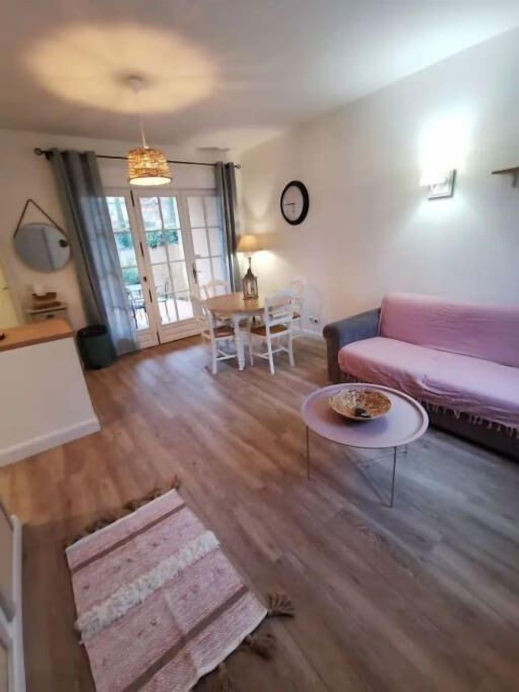Un salon avec un plancher en bois, un canapé rose, une table basse ronde et une table à manger avec des chaises.