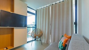 Un soggiorno moderno con un divano grigio, una televisione, una poltrona in vimini e un'ampia finestra con tende.