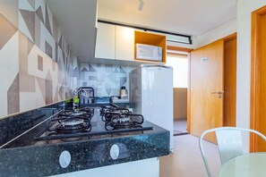 A modern kitchen with a gas stove, a microwave, and a refrigerator. There is a wooden door and a number '404' sign on the wall. - Apart na Praia de Maracaípe by Carpediem (Ipojuca)