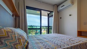 Una camera da letto con un'ampia finestra, un letto con lenzuola fantasia e un condizionatore d'aria a parete.