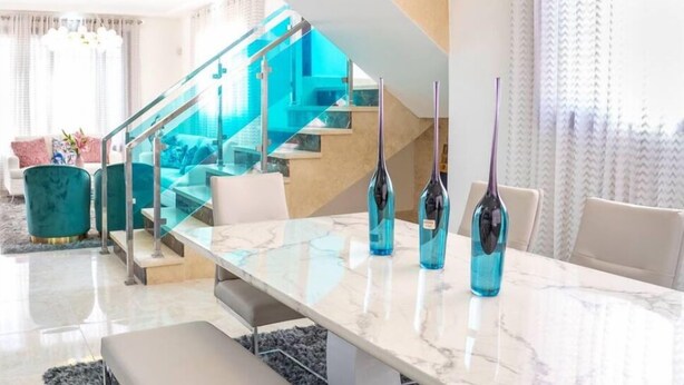 Uma sala de estar moderna com escada de vidro, mesa de centro de mármore e cadeiras em tom de verde-água.