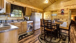 Interior de una cabaña de madera con una zona de cocina que incluye un refrigerador, estufa y armarios de madera.