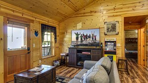 Interior acogedor de una cabaña con techo de madera, un sofá, un televisor y una máquina arcade de Pac-Man.
