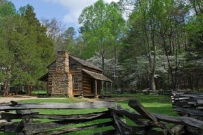 A rustic stone cabin surrounded by a wooden fence in a forested area.