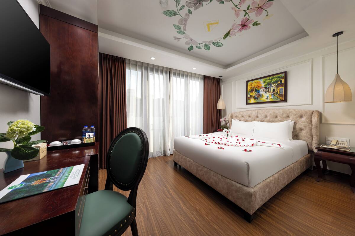 A hotel room with a large bed, a desk with a chair, a TV, and a painting on the wall.