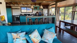 Une cuisine moderne avec un coin bar, un canap é turquoise agrémenté de coussins sur le thème de la mer et une table à manger.
