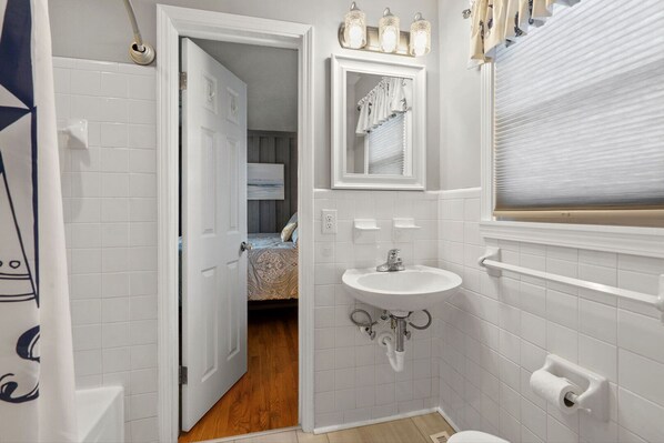 A bathroom with a white sink, a mirror, and a door leading to a bedroom. - Large channel home w/deck, close to beach and activities-in popular Cherry Grove (North Myrtle Beach)