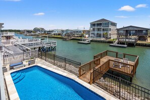 A waterfront property with a swimming pool, wooden deck, and multiple buildings with balconies. - Large channel home w/deck, close to beach and activities-in popular Cherry Grove (North Myrtle Beach)
