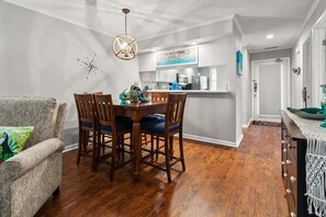 A dining area with a wooden table and chairs, a kitchen in the background, and a door leading to another room.