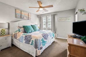 A bedroom with a bed, a nightstand, a TV, a ceiling fan, and artwork on the walls.