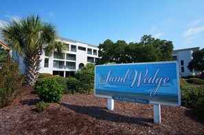 A sign for Sand Wedge at 201 N Hillside Drive, featuring a modern building with multiple balconies and lush landscaping.