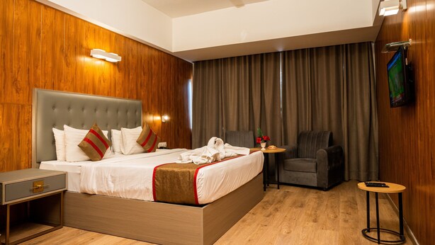 A hotel room with a large bed, a small table, a chair, a TV, and wooden paneling. - HOTEL ASRANI INTERNATIONAL (Hyderabad)